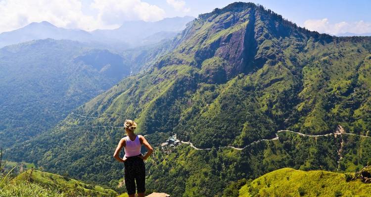 Persoon die op de rand van een klif staat en uitkijkt over de bergen.
