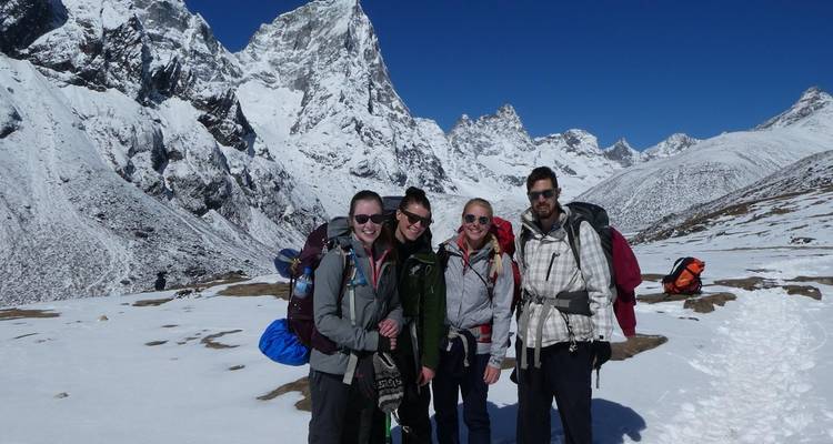 Groupe de randonneurs sur un sentier de montagne enneigé avec de hauts sommets en arrière-plan.