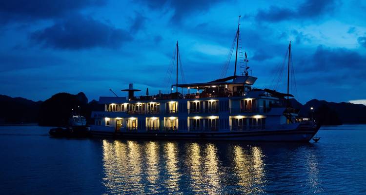 Beleuchtetes Kreuzfahrtschiff bei Nacht, das sich im Wasser spiegelt.