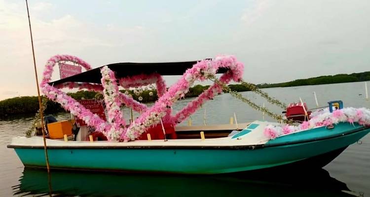 Petit bateau à moteur turquoise décoré de fleurs roses et blanches flottant sur un lagon calme.