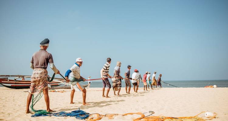 Groupe de pêcheurs tirant des filets sur une plage de sable.
