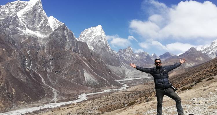 Man posing with arms outstretched in front of snowy mountains.