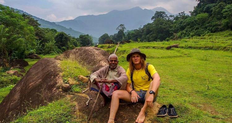 Twee mensen die op een rots zitten in een groene vallei met bergen op de achtergrond.