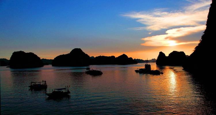 Hermoso atardecer sobre una bahía con pequeños barcos silueteados contra el agua.