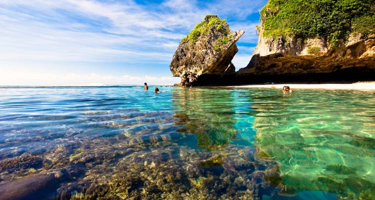 Nadadores en el mar turquesa cristalino cerca de una formación rocosa.