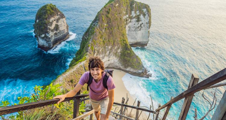 Hombre subiendo escaleras con un fondo escénico de acantilado.