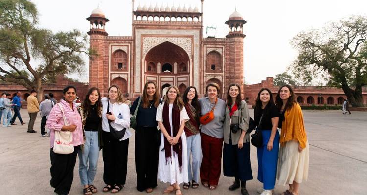 Eine Gruppe von Frauen posiert lächelnd vor dem verzierten roten Sandsteintor des Taj Mahal-Komplexes.