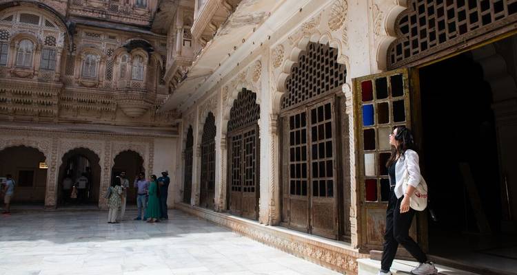 Besucher wandeln durch den schattigen Marmor-Innenhof eines kunstvoll geschnitzten Palastes in Jodhpur.