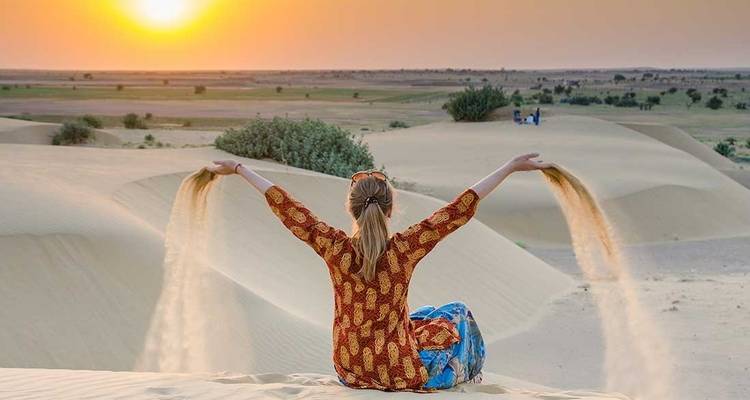 Frau, die bei Sonnenuntergang in einer Wüste mit Sand spielt.