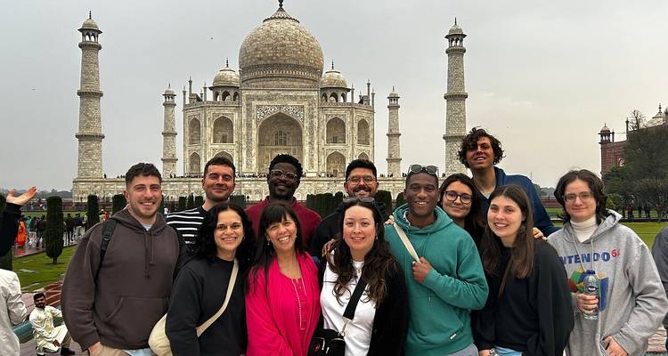 Gran grupo de turistas sonriendo frente al Taj Mahal en un día nublado.