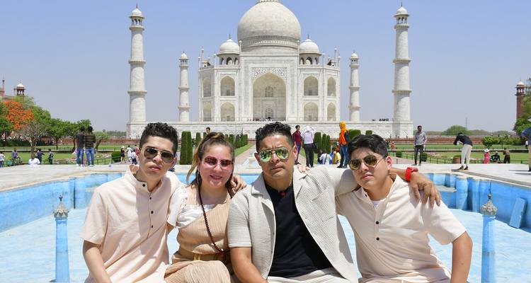 Jóvenes amigos posan del brazo frente al Taj Mahal bajo un cielo azul brillante.