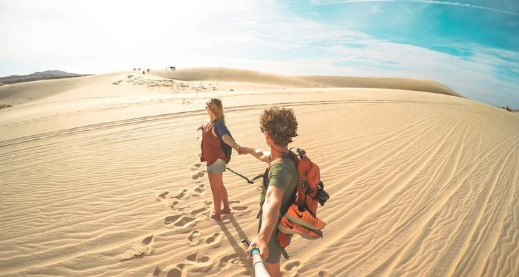 Pareja caminando en dunas de arena con un cielo azul despejado.