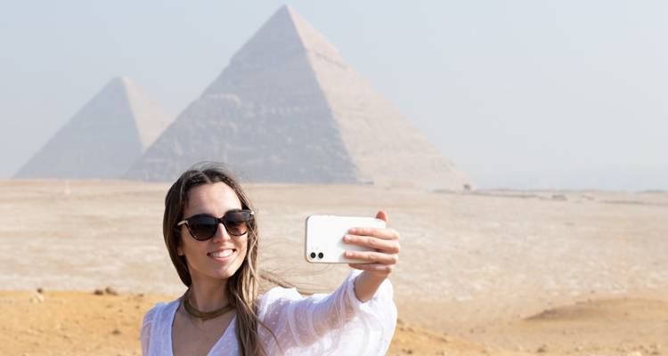 Person, die ein Selfie mit Pyramiden im Hintergrund macht.
