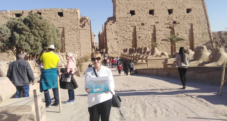 A person holding a sign in front of a historic temple with tourists walking around.