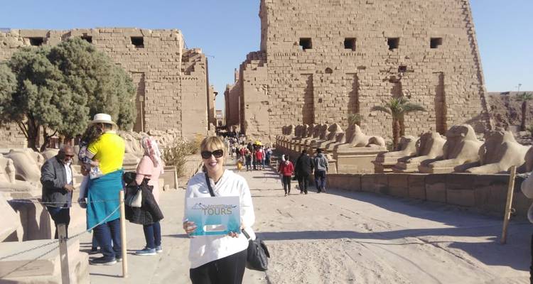 A person holding a sign in front of a large ancient temple with other tourists visible.