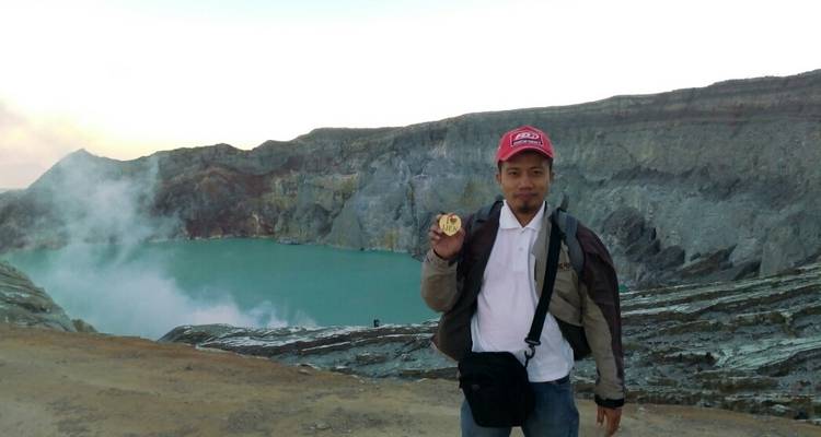 Man die een steen vasthoudt met een vulkanische krater op de achtergrond.