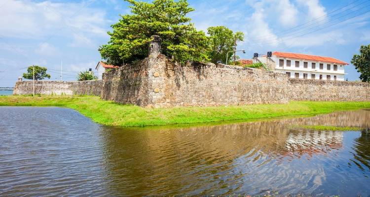 Ancienne fortification près de l'eau avec de la verdure et un ciel bleu.