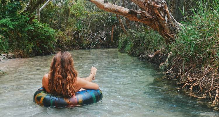 Personne flottant sur une bouée gonflable dans un ruisseau limpide entouré de verdure.