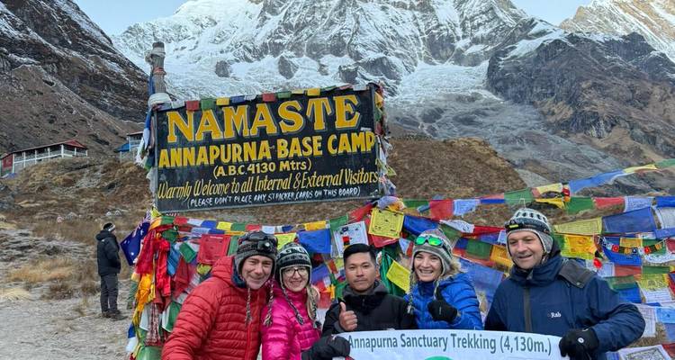 Groupe de randonneurs au camp de base de l'Annapurna avec un panneau de bienvenue.