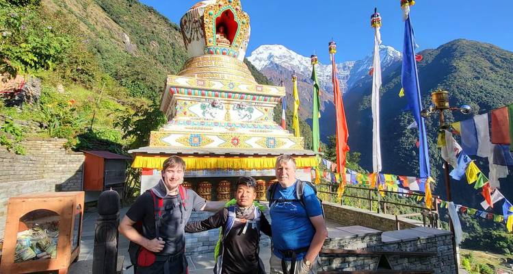 Trois randonneurs posant près d'un stupa avec des montagnes en arrière-plan.