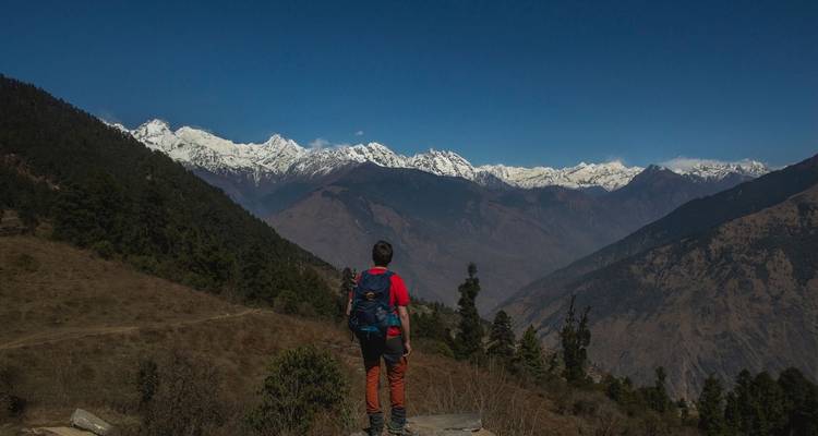 Une personne en veste rouge regardant une chaîne de montagnes enneigées.