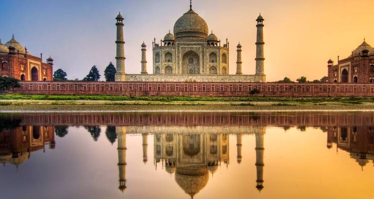 The Taj Mahal reflected in a calm river during sunset.