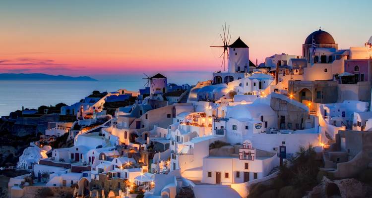 Pueblo de Santorini al atardecer con molinos de viento y edificios blancos.