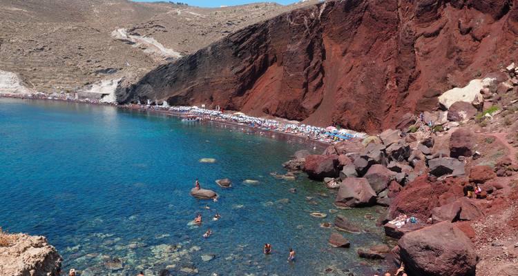 Playa con acantilados rojos y gente nadando en el mar.