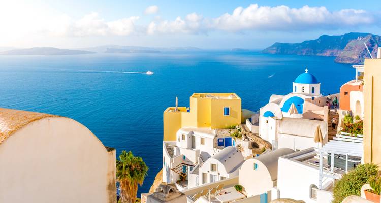Vue classique de carte postale de maisons blanchies à la chaux et d'églises aux dômes bleus s'étalant en cascade le long des falaises d'Oia, Santorin, face à la profonde mer Égée bleue.