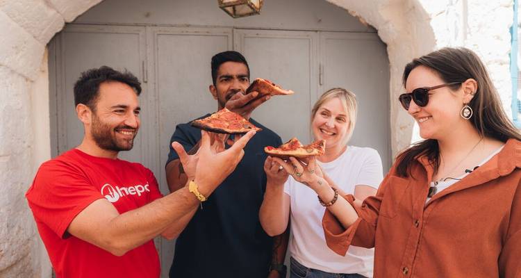 Des voyageurs lèvent des parts de pizza pour porter un toast de célébration devant une arche de pierre.