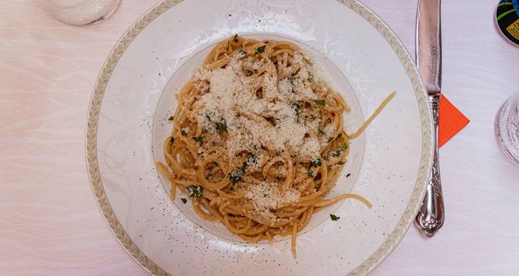 Une vue de dessus rapprochée d'une assiette de spaghetti généreusement saupoudrée de pecorino et d'herbes.