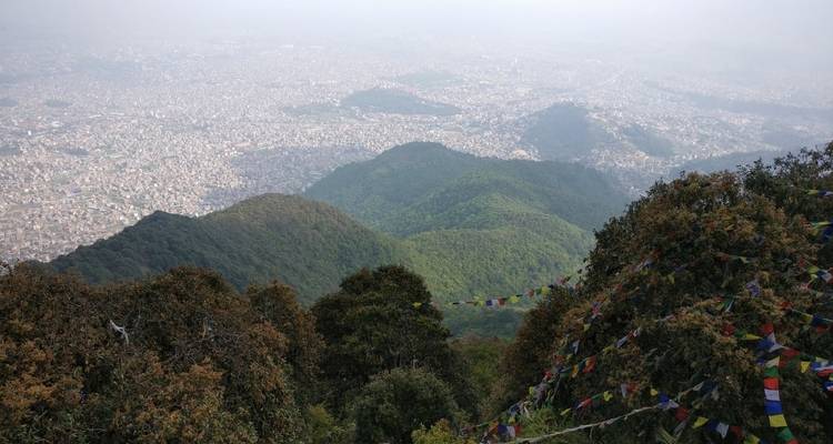 Bergachtig landschap met gebedsvlaggen en uitzicht op verre stad.