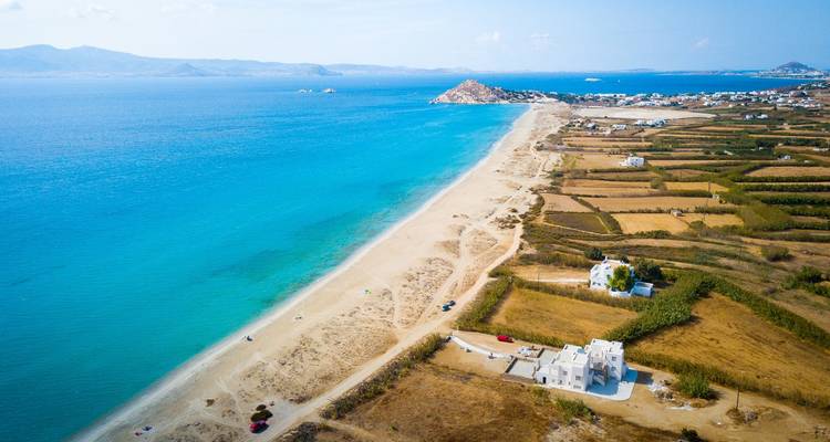 Playa de arena con aguas turquesas que se extienden hacia un paisaje montañoso distante.