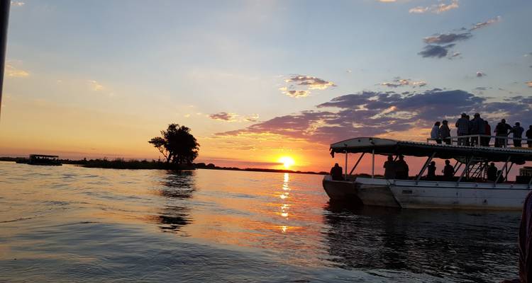Silhouetten von Menschen auf einem Boot, die einen Sonnenuntergang über dem Wasser genießen.