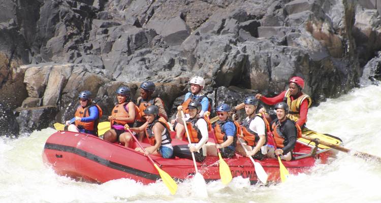 Eine Gruppe von Menschen beim Rafting in Stromschnellen mit felsigen Klippen im Hintergrund.