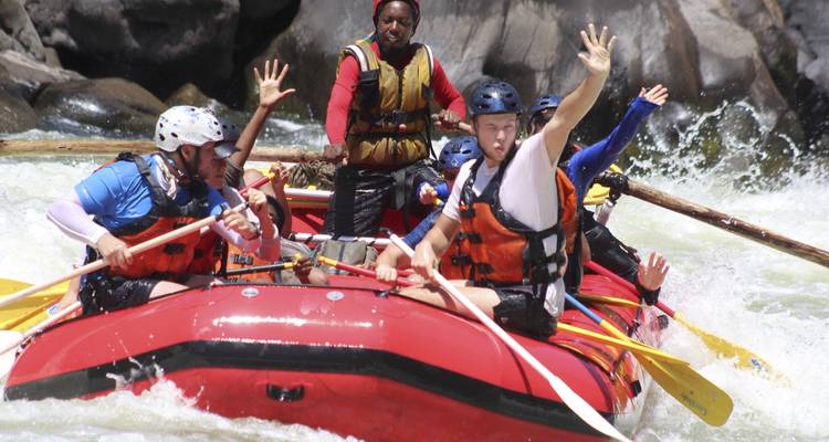 Menschen auf einem Floß, die ihre Hände heben, während sie Stromschnellen bewältigen.