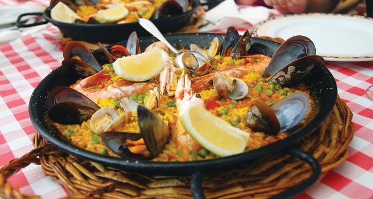 Paelleras llenas de mariscos, guisantes y gajos de limón servidas sobre un mantel a cuadros.