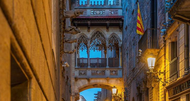El Puente de los Suspiros gótico atraviesa un callejón estrecho en el barrio medieval de Barcelona iluminado al anochecer.