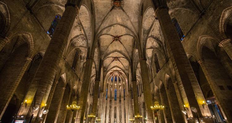 Gran nave abovedada de una catedral gótica iluminada cálidamente, mostrando columnas de piedra elevadas y candelabros.