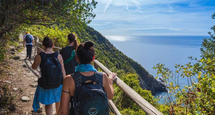 Des randonneurs avec des sacs à dos suivent un sentier côtier surplombant une mer bleue scintillante sous un ciel dégagé.