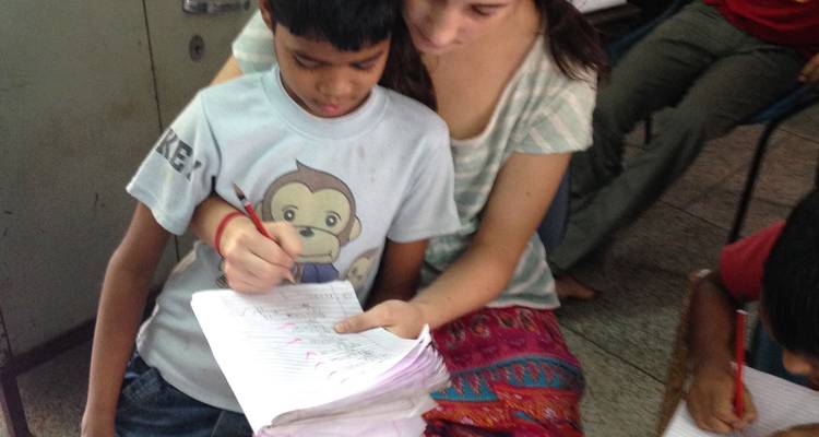 Un bénévole aide un jeune garçon à pratiquer l'écriture dans un cahier d'exercices à l'intérieur d'une salle de classe.