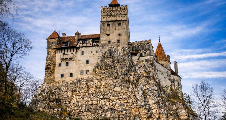 Bran Castle perched on a rocky cliff with blue skies overhead.