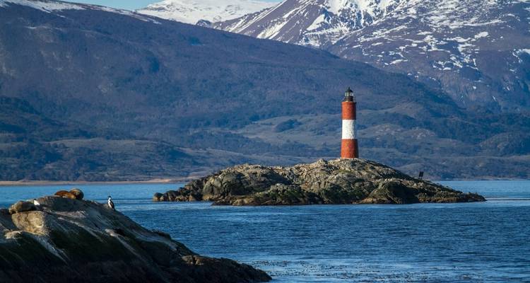 Leuchtturm auf einer kleinen Insel mit Bergen im Hintergrund.