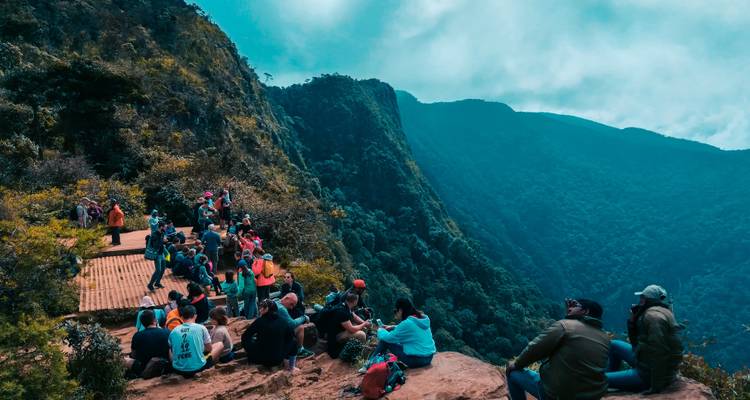 Menschenmenge auf einem Bergaussichtspunkt, umgeben von üppigen Hügeln.