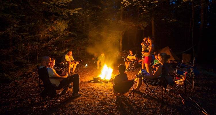Gruppe von Menschen, die sich nachts um ein Lagerfeuer in einem Wald versammelt haben.