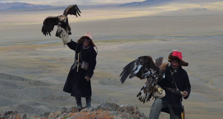Two people with eagles on a rocky terrain.