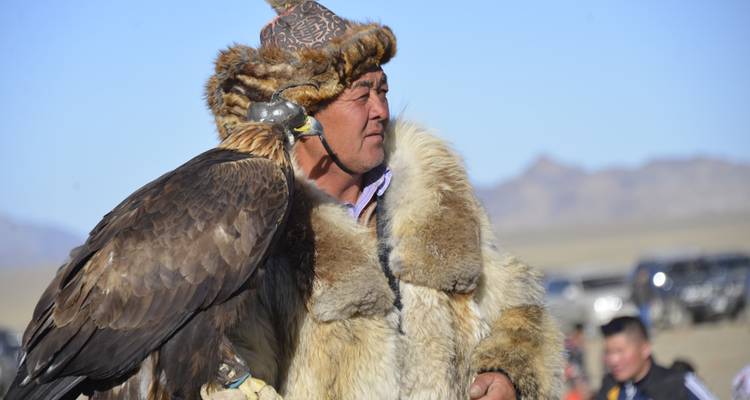 Man wearing traditional attire holding an eagle.