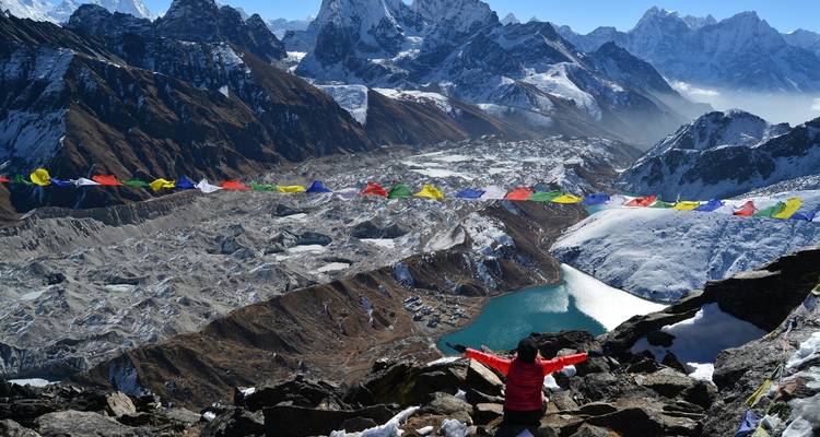 Persoon met opgeheven armen bij vlaggenslinger en besneeuwde bergtoppen.
