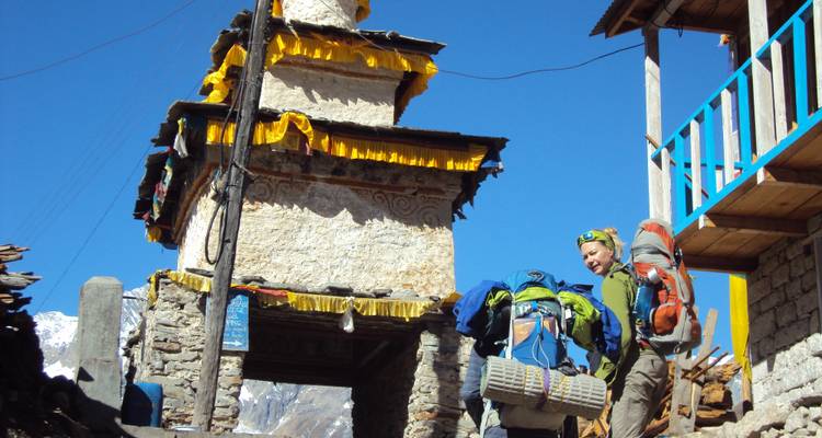 Hikers passing through an archway in a village with mountains in the background.