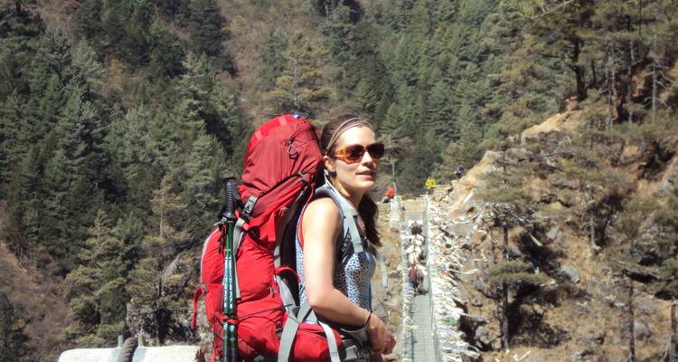 Hiker posing on a suspension bridge in a forest area.